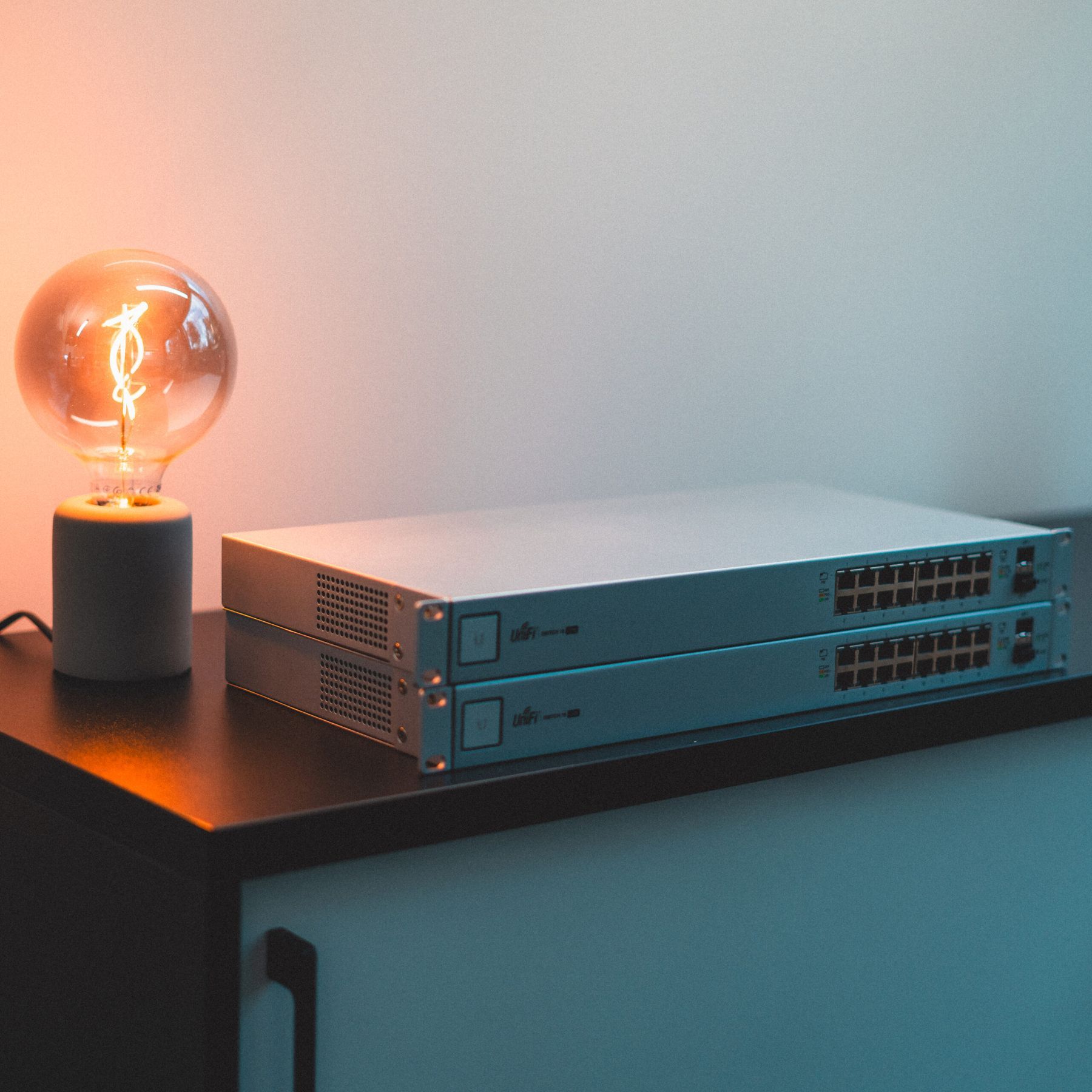 Två switchar från Ubiquiti på ett skåp bredvid en tänd lampa